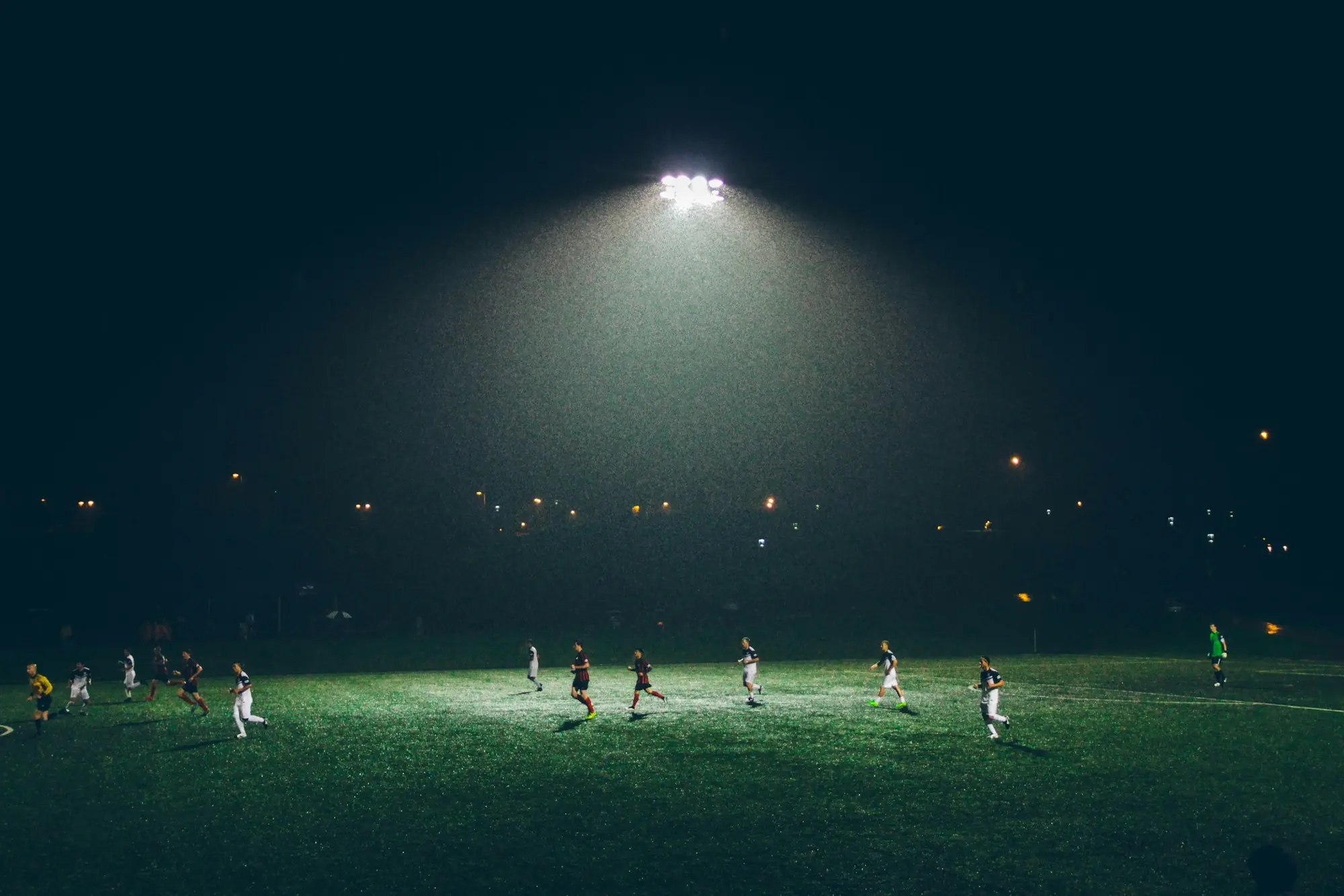 Partido de fútbol nocturno en una cancha iluminada por reflectores
